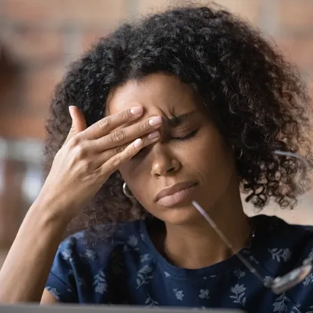 A woman touching her forehead with a pained expression, suggesting a headache or migraine