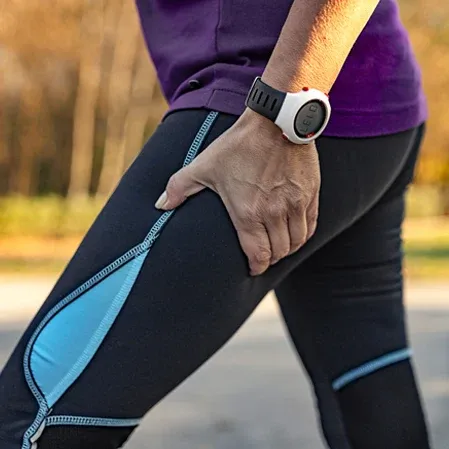 A person outdoors holding the back of their thigh, indicating sciatic nerve pain or leg discomfort.