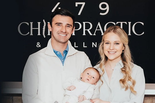 Dr. Zac Pinter and wife holding a baby, standing in front of 479 Chiropractic & Wellness clinic sign.